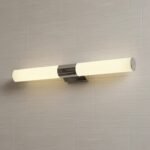 Aplique de pared LED moderno cromado con luz cálida sobre fondo de baldosas claras, ideal para baño o dormitorio.