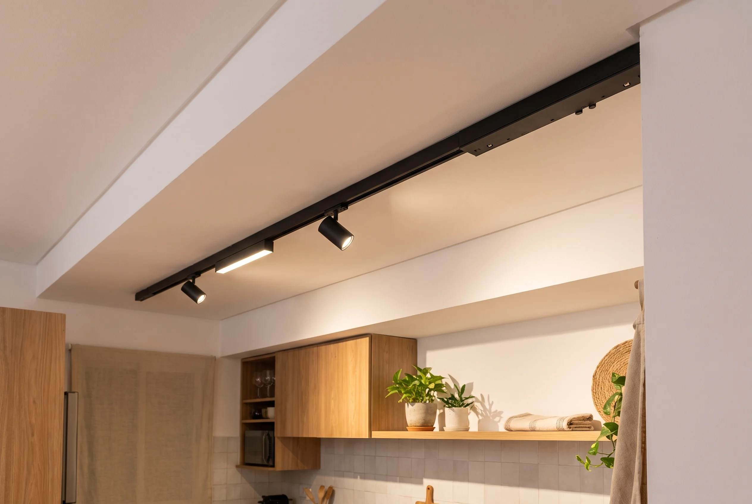 Fuente de 200W integrada en línea al riel magnético negro sobre el techo de una cocina moderna argentina, con spots y difusor lineal encendidos en luz cálida 3000K